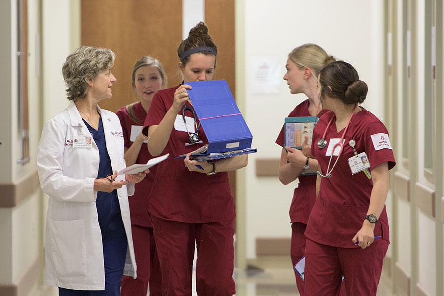 College of Nursing students walk with their professor and look over clinical notes after class