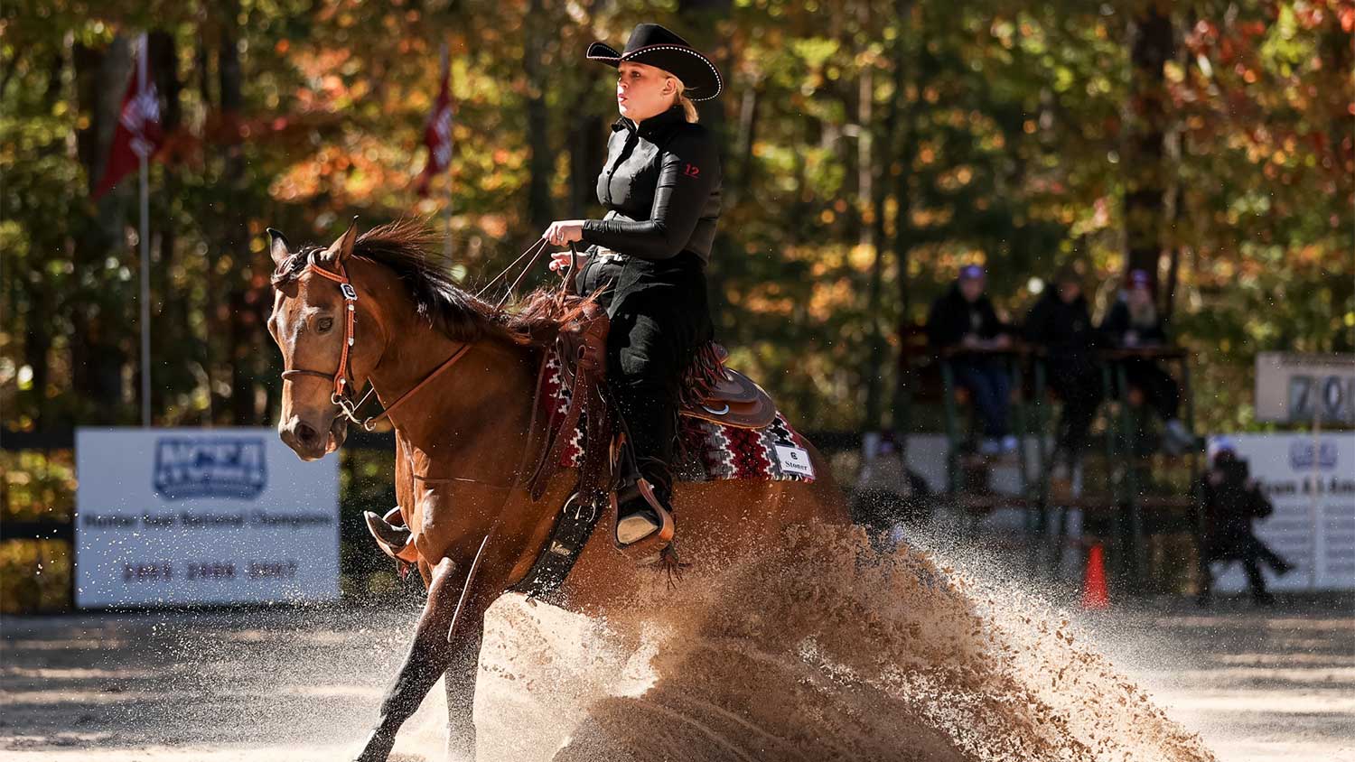 A woman rides a horse making a tight turn and kicking up sand