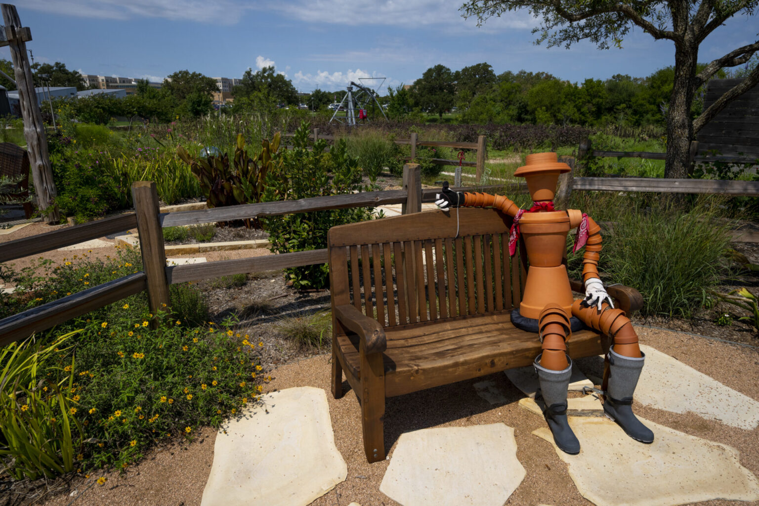 terracotta pot sculpture sits on a bench in front of the cottage gardens