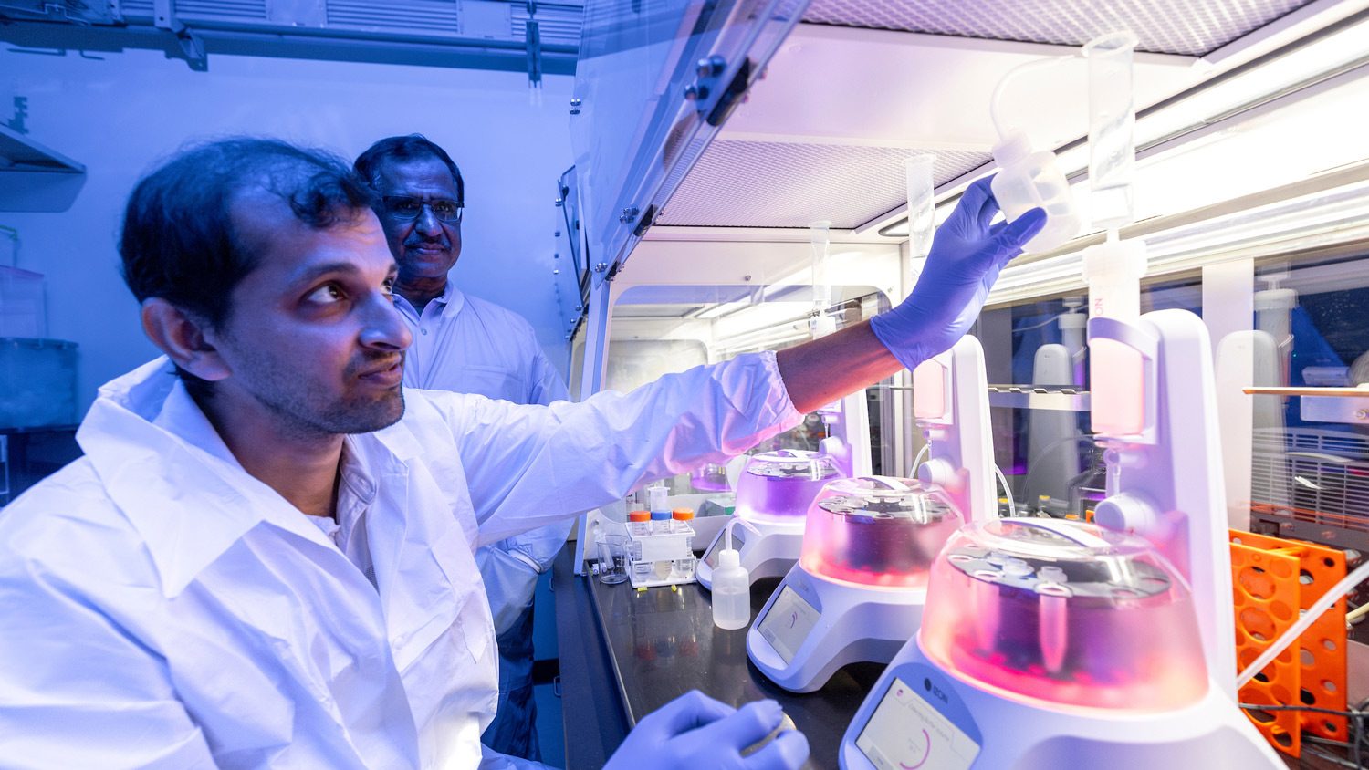 Researchers in lab coats interact with research equipment.