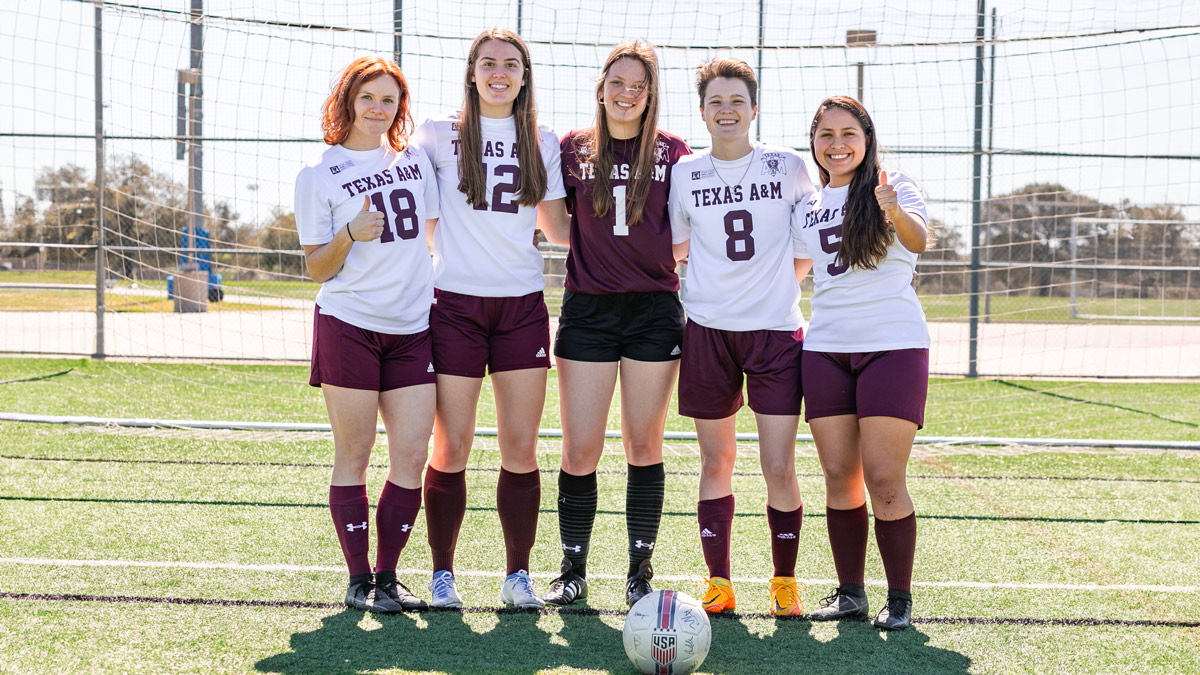 Members of the Corps women's soccer team pose in front of the soccer goal