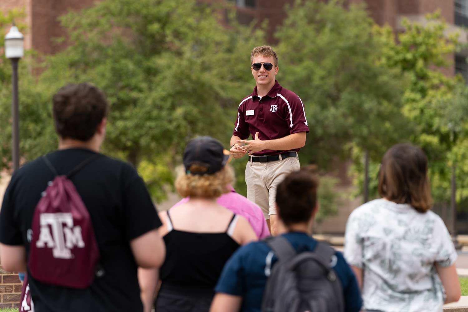 Texas A&M tour guide stands on a bench to address the crowd of prospective students